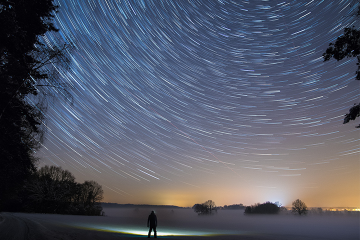 Photo of man standing in field at night looking at stars