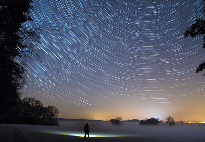 Photo of man standing in field at night looking at stars